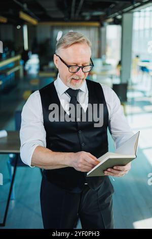 Männlicher Finanzier mit grauem Haar, der Finanzberichte und Verträge überprüft, Erwachsener Chef, der am Arbeitsplatz mit Papieren arbeitet. Stockfoto