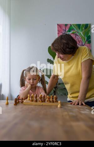 Konzentriert, aber fröhlich, lachen Großmutter und Enkelin gemeinsam Schach. Hochwertige Fotos Stockfoto