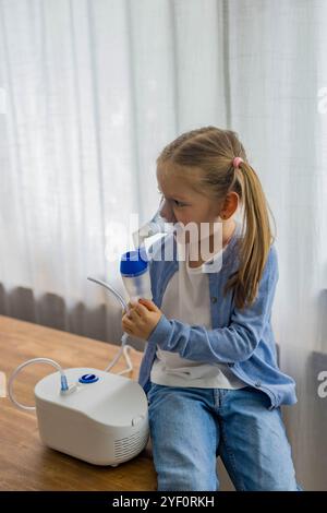 Zu Hause atmet ein 5-jähriges Mädchen durch einen Vernebler und konzentriert sich auf ihre Inhalationstherapie. Hochwertige Fotos Stockfoto