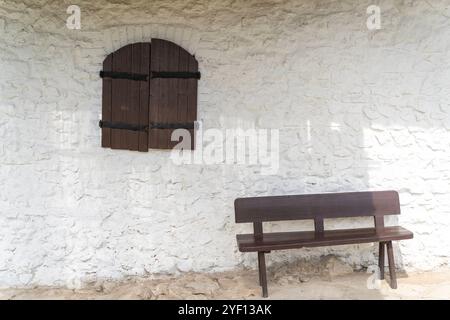 Altes, weißes Landhaus mit rustikalen braunen Holzläden und Holzbank Stockfoto