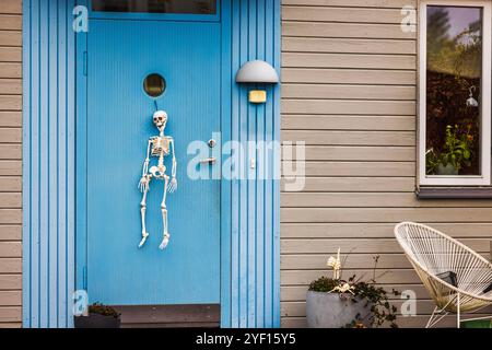 Halloween Skelett Dekoration hängt an der blauen Tür des Hauses mit Topfpflanzen, die festliche und gruselige Atmosphäre schaffen. Stockfoto