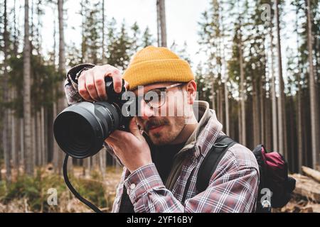 Porträt eines Fotografen. Ein junger Hipster schaut durch das Objektiv im Wald in die Kamera Stockfoto