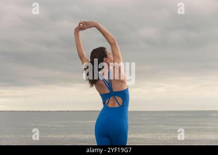 Sportliche Schwimmerin, die am Strand einen Arm über dem Kopf streckt Stockfoto