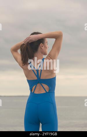 Sportliche Frau, die ihre Haare zubindet, bevor sie sich anstrengt oder wild an der Küste schwimmt Stockfoto