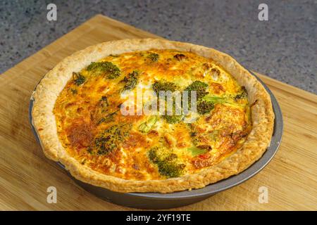 Ein Nahaufnahme einer Quiche mit goldener Kruste, gefüllt mit Brokkoli-Röschen und einer käsigen, cremigen Füllung, die perfekt auf einem hölzernen Schneidebrett gebacken wurde. Stockfoto