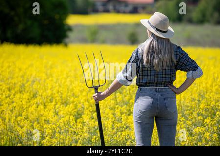 Eine Frau steht in einem pulsierenden Feld, hält eine Gabel und nimmt sich fröhlich auf das ländliche Leben und die Natur ein Stockfoto