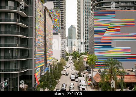 Miami, Florida, USA - 4. Dezember 2023: Verkehr und Fußgänger auf einer Straße in der Innenstadt zwischen Gebäuden mit farbigen Außenwänden. Stockfoto