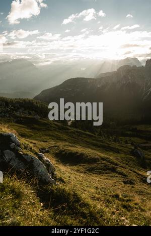 Die Sonne scheint hell durch die flauschigen Wolken, die über den majestätischen Bergen am fernen Horizont schweben Stockfoto