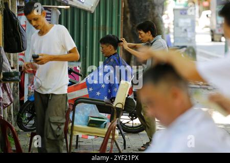 Hanoi, Vietnam - 22. Juli 2023: Friseure schneiden die Haare von Kunden in einem Friseursalon auf dem Bürgersteig. Stockfoto