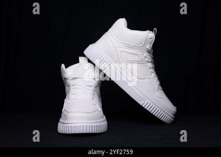 Studio-Aufnahme mit weißen High-Top-Sneakers auf schwarzem Hintergrund, die moderne modische Schuhe darstellen Stockfoto