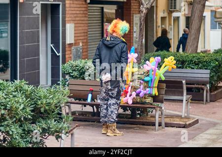 Unerkennbarer Clown mit gedrehtem Rücken, besorgt und mit den Händen hinter dem Rücken auf einige Ballons mit verschiedenen und bunten Formen auf einem P Stockfoto