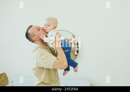 Der junge lächelnde Vater spielt mit seinem neugeborenen Sohn. Dad und kleiner Sohn. Stockfoto