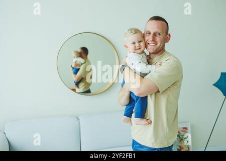 Der junge lächelnde Vater spielt mit seinem neugeborenen Sohn. Dad und kleiner Sohn. Stockfoto