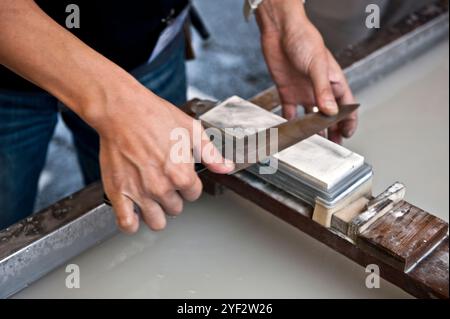 Person, die in Seki City, Gifu, Japan, ein Küchenmesser oder „Hocho“ mit einem Schleifstein schärft. Stockfoto