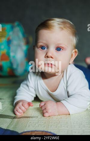 Ein viermonatiger Junge liegt auf einem Teppich auf dem Boden und spielt mit Spielzeug. Das Kind hält den Kopf. Ein Baby lernt, auf dem Boden zu krabbeln Stockfoto