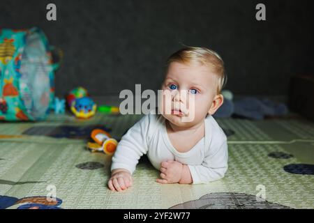 Ein viermonatiger Junge liegt auf einem Teppich auf dem Boden und spielt mit Spielzeug. Das Kind hält den Kopf. Ein Baby lernt, auf dem Boden zu krabbeln Stockfoto