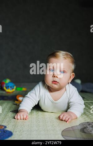 Ein viermonatiger Junge liegt auf einem Teppich auf dem Boden und spielt mit Spielzeug. Das Kind hält den Kopf. Ein Baby lernt, auf dem Boden zu krabbeln Stockfoto