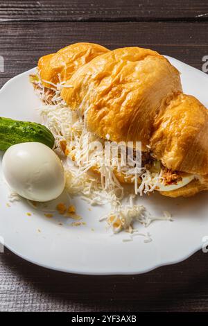 Croissant-Sandwich mit Thunfisch, Ei, Gurke und Käse auf einem weißen Teller Stockfoto