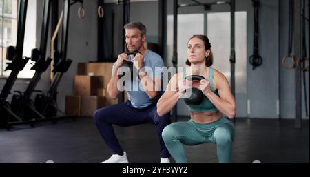 Fitnesspaar Im Fitnessstudio. Training Mit Kettlebell, Der Squats Macht Stockfoto