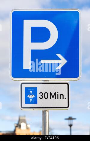 Ein blaues Parkschild, das eine Parkdauer von 30 Minuten anzeigt, mit einem Pfeil nach rechts. Dieses deutsche Straßenschild zeigt zeitlich begrenzte Parkzonen Stockfoto