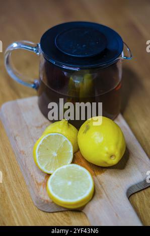 Teekanne aus Glas mit Tee mit gehackter Zitrone auf Schneidebrett in der Küche. Hochwertige Fotos Stockfoto