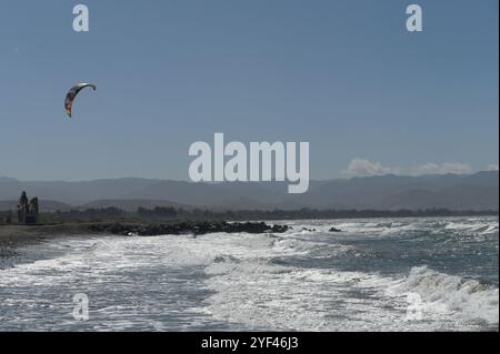 Ein talentierter Kitesurfer reitet an einem sonnigen Nachmittag auf den Wellen und zeigt seine Fähigkeiten vor einer wunderschönen Kulisse. Stockfoto