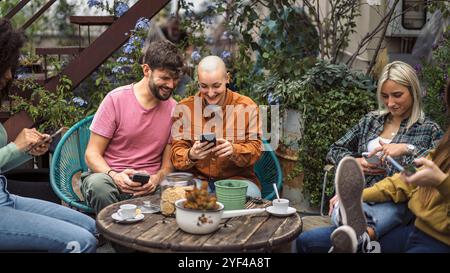Millennials-Freunde genießen zwangloses Treffen am Wochenende auf der Gartenterrasse, teilen soziale Medien und trinken Kaffee mit Snacks. Natürlicher, authentischer Lifestyle Stockfoto