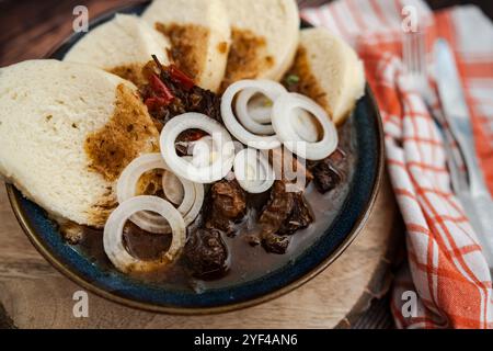 Die Szene zeigt ein traditionelles tschechisches Rindergulasch, serviert mit Brotknödeln und Zwiebeln. Dieses klassische Gericht im Pub-Stil wird in einem rustikalen Dinin serviert Stockfoto