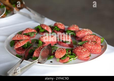 Kleine Sandwiches mit Rote-Bete-Brot, Lammprosciutto und Maissalat werden auf einem weißen Teller bei einer Veranstaltung mit Catering serviert Stockfoto