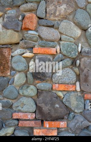 Wand aus einer Kombination von Steinen und Ziegeln in verschiedenen Größen und Formen. Die Steine sind meist grau-grün, während die Steine rot-orange sind. Stockfoto