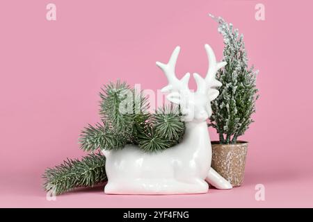 Weiße keramische Weihnachts- oder Winterdekoration Hirschfigur mit Tannenzweigen und kleinem Baum auf rosa Hintergrund Stockfoto