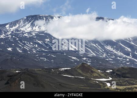 Vulkanische Landschaft der Kamchatka Halbinsel: Schöner Sommerblick auf den Kegel des aktiven Vulkans Plosky Tolbachik und Wolken, die teilweise die Spitze des vol verbergen Stockfoto