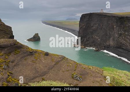 Klippen und Küste mit Meer, unter bewölktem Himmel mit Blick auf Leuchtturm, Dyrholafjara, Felsentor Dyrholaey oder Dyrholaey, Südküste, Island, EUR Stockfoto