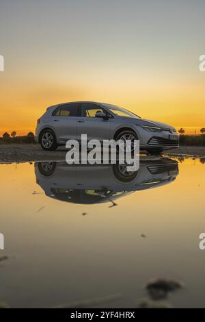 Silbernes Auto spiegelt sich bei Sonnenuntergang in einer Wasserpfütze, atmosphärischer Himmel in Gelb- und Orangetönen, VW Golff Diesel, Calw, Schwarzwald, Deutschland, Eur Stockfoto