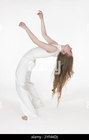 In voller Länge, barfuß, junge Frau mit geschlossenen Augen, die Spaß beim Bücken nach hinten auf weißem Hintergrund hat. Seitenansicht der flexiblen Blondie fema Stockfoto