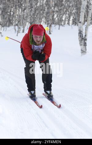 PETROPAVLOVSK, HALBINSEL KAMTSCHATKA, RUSSLAND, 10. FEBRUAR 2018: Skifahrer in rot-schwarzem Sportanzug fährt vom Berg auf Skiern im Winterwald. A Stockfoto