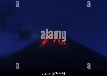 Wunderschöner Nachtanblick auf aktiven Vulkanausbruch, glühende rote Lavaflüsse, die aus dem Vulkankrater ausbrechen, blauer Himmel in der Abenddämmerung. Berglandschaft bac Stockfoto