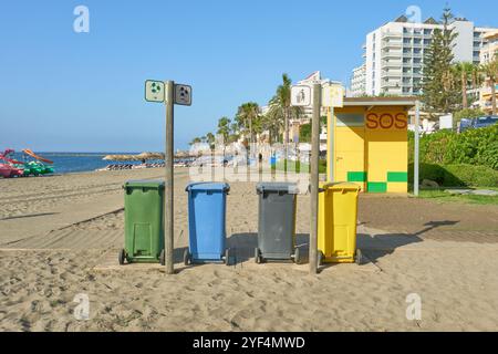 Vier Mülltonnen am Sandstrand von Torre Bermeja in Benalmadena, Malaga, Andalusien, Spanien. Neben einer Rettungsstation, eingerahmt von einem Küstenzit Stockfoto