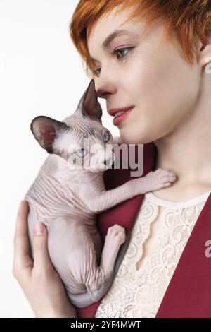 Hipster junge Rotschopf Frau sanft umarmt Canadian Sphynx Cat. Selektiver Fokus auf Jungtiere, geringe Schärfentiefe. Nette Frau in roter Jacke gekleidet. S Stockfoto