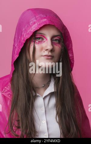 Porträt informelle junge Erwachsene Frau mit rosa Bühnenbild mit Pailletten und Pfeilen auf dem Gesicht, Blick in die Kamera. Frau in rosafarbener Jacke mit Stockfoto