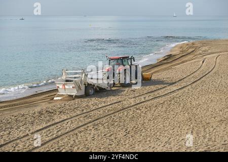 Strandreinigungstraktor mit Ausrüstung an einem Sandstrand in der Nähe des Wassers, mit ruhigem Mittelmeer. In Benalmadena, Malaga, Andalusien, Spanien Stockfoto