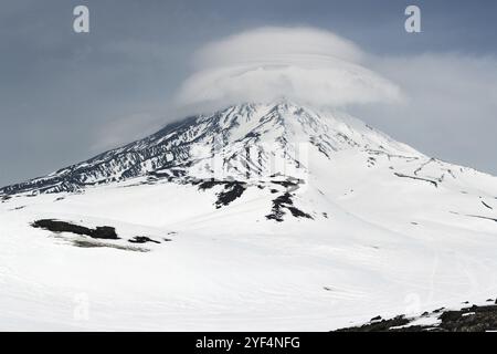 Winterliche Berglandschaft von Kamtschatka: Blick auf den aktiven Korjakski-Vulkan (Korjakskaya Sopka) und die wunderschönen Lentikularwolken, die die Spitze der umhüllen Stockfoto