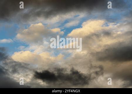 Golden Fluffy Clouds von verschwindenden Strahlen bei Sonnenuntergang und dunklen Gewitterwolken schwimmend über sonnigen blauen Himmel Sommer Wetter zu ändern beleuchtet. Stunni Stockfoto