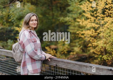 Porträt einer niedlichen jungen Frau in lässiger Kleidung im Herbst, stehend auf der Brücke vor dem Hintergrund eines Herbstparks und Flusses. Hübsche weibliche Spaziergänger in Par Stockfoto