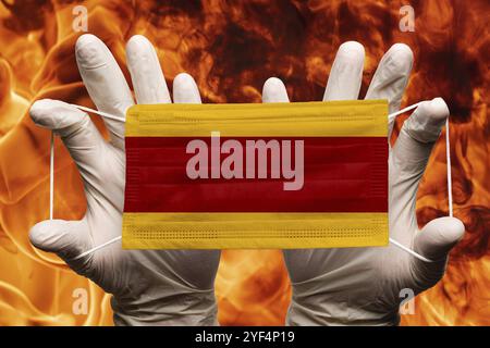 Arzt hält in weißen Handschuhen Schutz medizinische Gesichtsmaske, Atembandage mit Spanien Nationalflagge überlagert auf Maske. Konzept zu bac Stockfoto
