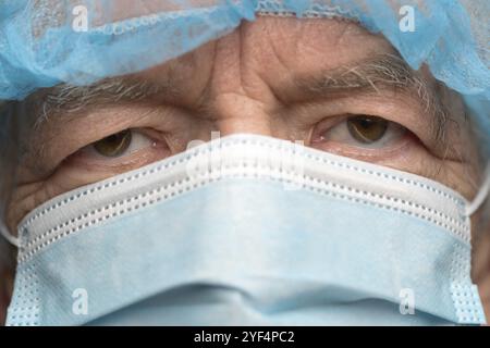Nahaufnahme Porträt eines traurigen älteren Erwachsenen in chirurgischer Gesichtsmaske mit Ohrbügeln, bedeckt Nase von SARS, virulent infektiöse Krankheit Corona vir Stockfoto