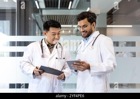 Ärzte im Gespräch mit dem digitalen Tablet im Krankenhaus. Professionelle Zusammenarbeit hebt Teamwork, Gesundheitswesen und Technologie hervor. Medizinische Fachkräfte tauschen Erkenntnisse aus und verbessern die Patientenversorgung. Stockfoto