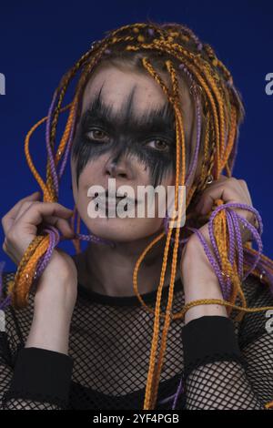 Kinoporträt einer süßen jungen Frau mit orangefarbenem Dreadlocks-Haarschnitt und grauenschwarzem Bühnenschminke auf dem Gesicht. Vorderansicht, Studioaufnahme Stockfoto