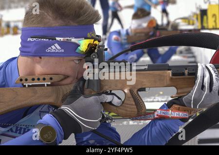 Sportliche Biathleten-Gewehrschießen, Zielen, Nachladen des Gewehrs in Bauchlage. Biathlet Kozulin Aleksander im Schießstand. Juniorbiathlon-Wettkämpfe Stockfoto