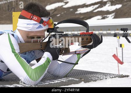 Sportlicher Biathlet zielt, Gewehrschießen, Nachladen des Gewehrs in Bauchlage. Biathlet Vladislav Zlobin im Schießstand. Junior-Biathlon-Wettkämpfe Stockfoto